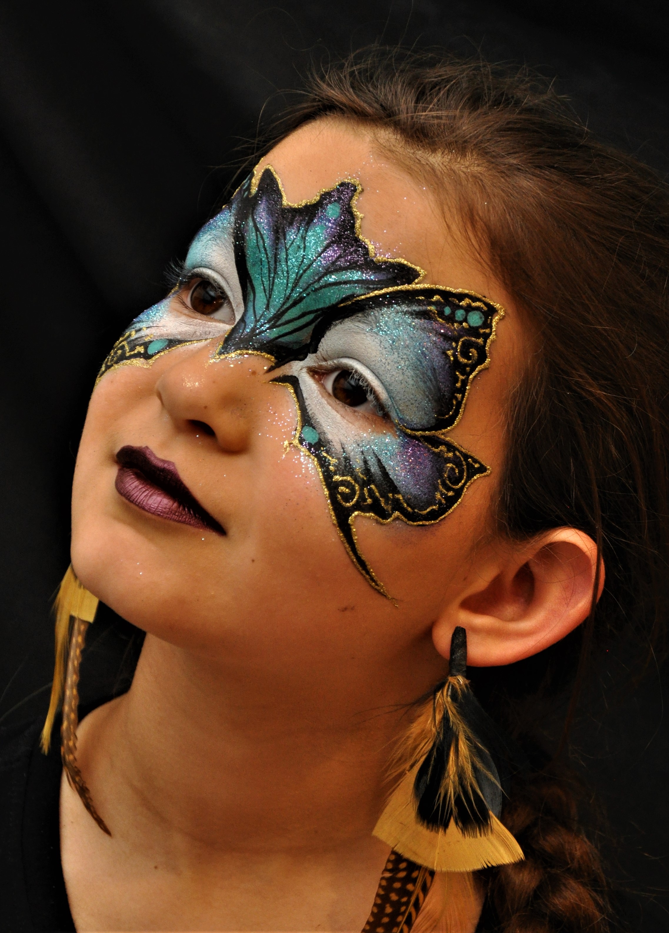 Youg girl with face painting of a mask around her eyes in blue black and gold that resembles a butterflies wings